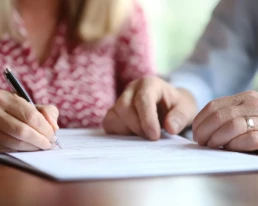 una pareja felizmente firmando papeles de prestamo hipotecario en una mesa de cierre con un prestamista mini